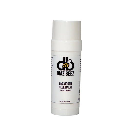 A white cylindrical container of BeeSMOOTH Heel Balm by Diaz Beez stands upright against a plain background. The label features a black and yellow bee logo and text indicating it's a tea tree and lavender scented balm for dry, cracked feet, weighing 2 oz (59 ml).