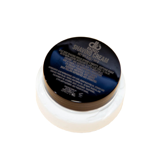 A sleek round black container labeled "Diaz Beez Shaving Cream with Aloe Vera" is elegantly placed on a white surface. The container comes with a screw-on lid, and the product details prominently highlight the soothing benefits of Vitamin E on the top label.